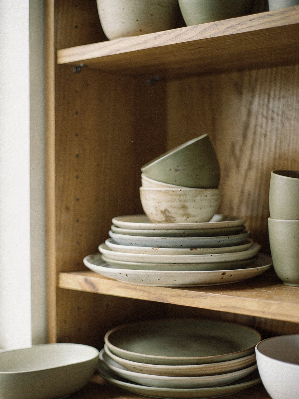 Pilhas de pratos e bowls de cerâmica artesanal em tons de areia e verde-oliva